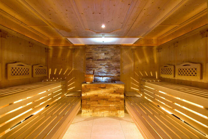 Beleuchtete Bio-Sauna mit viel Holz und Wandverkleidung aus Steinen