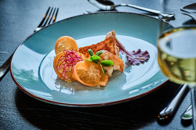 Fein angerichtete Garnelen mit Gemüseröllchen und Gelee auf türkisfarbenem Teller.