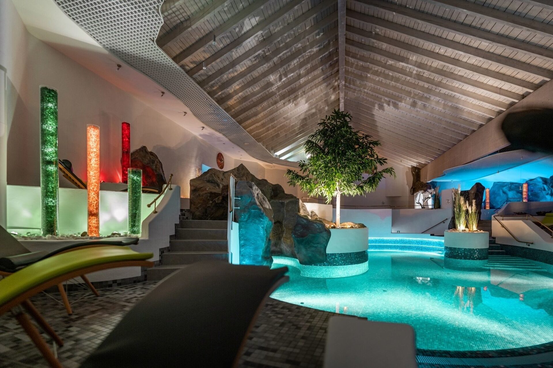 Stimmungsvolle Poollandschaft am Abend mit sanfter Beleuchtung und Natursteinelementen.