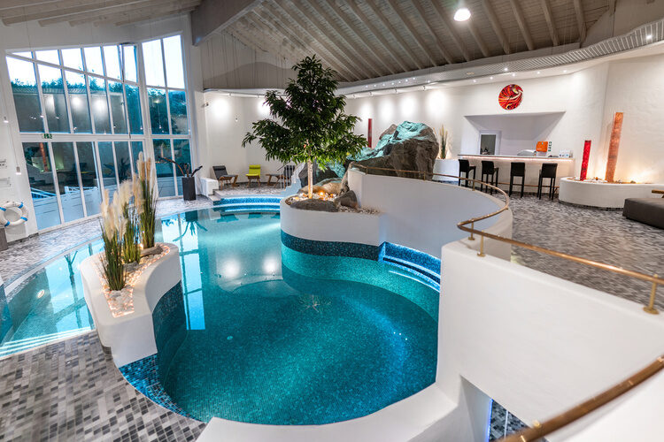 Innenpool mit Bar, Pflanzeninsel und Panoramafenstern in modernem Ambiente.