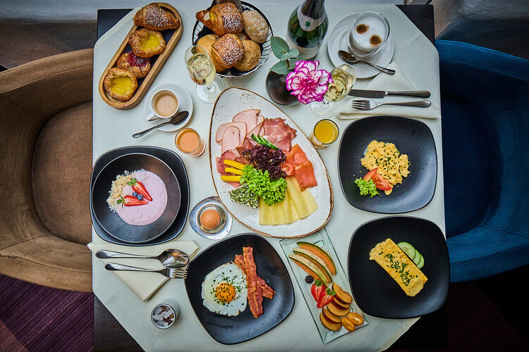 Reich gedeckter Frühstückstisch mit Aufschnitt, Eierspeisen, Joghurt und frischem Obst.