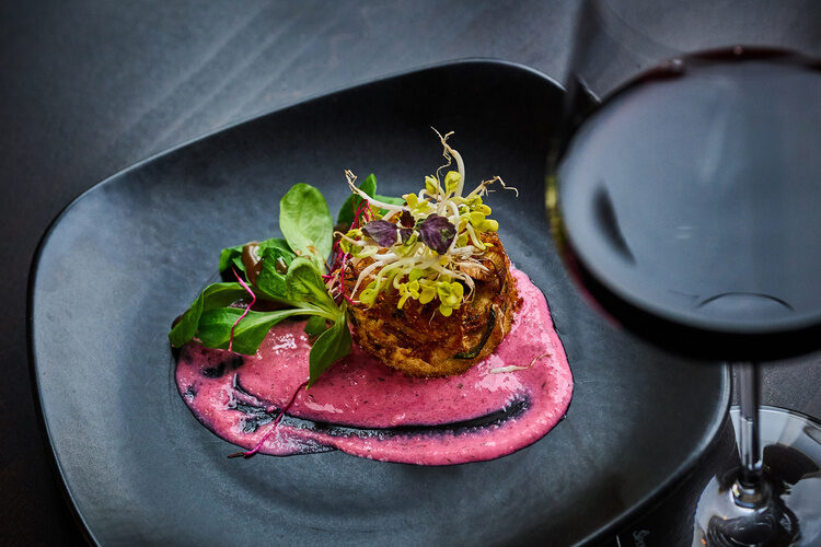 Gourmetgericht mit Sprossen und rosa Soße auf dunklem Teller serviert.