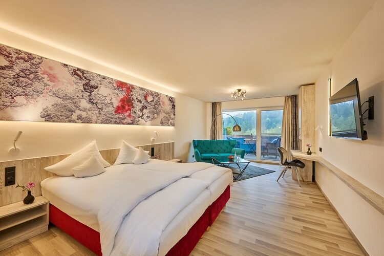 Großzügiges Hotelzimmer mit Doppelbett, Sitzecke und Balkonblick ins Grüne.