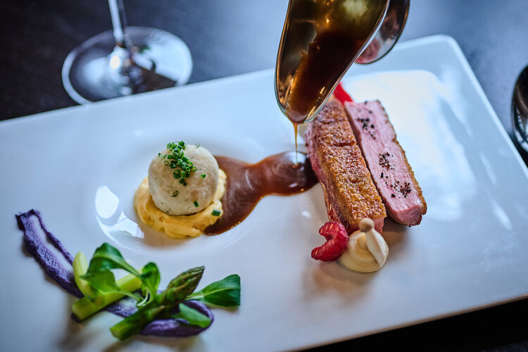 Entenbrust mit Sauce, Kartoffelknödel und Gemüse auf weißem Teller angerichtet.