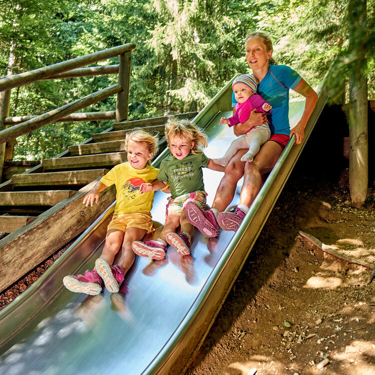 Frau mit drei Kindern rutscht im Waldspielgelände