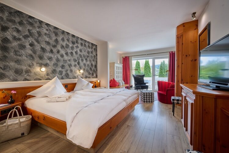 Elegantes Hotelzimmer mit Doppelbett, Holzverkleidung, Sitzbereich und Gartenausblick.
