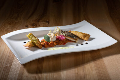 Ein wei&szlig;er Teller mit Fisch und Gem&uuml;se auf einem runden Tischset aus Holz.