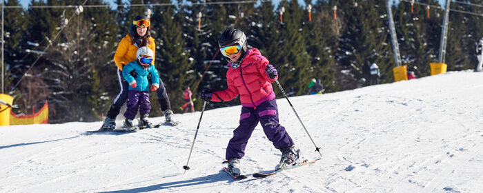 Mädchen beim Skifahren mit Frau und Kleinkind im Hintergrund beim Lernen des Skifahrens