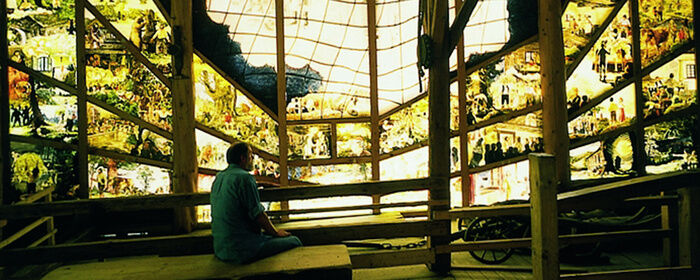 Mann sitzt in der Gläsernen Scheune und begutachtet die Glasmalereien