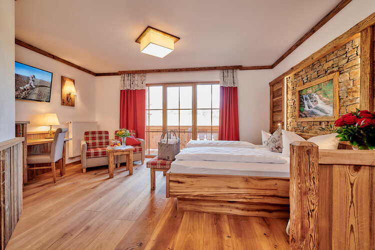 Ein stilvoll gestaltetes Schlafzimmer im Tonihof mit Holzboden und roten Vorhängen.