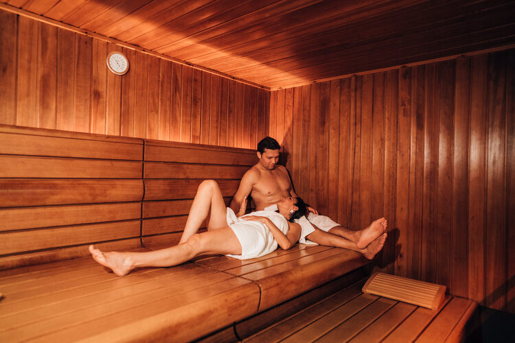 Paar entspannt in Sauna mit warmem Holzinterieur, gedimmtes Licht, intime Atmosphäre.